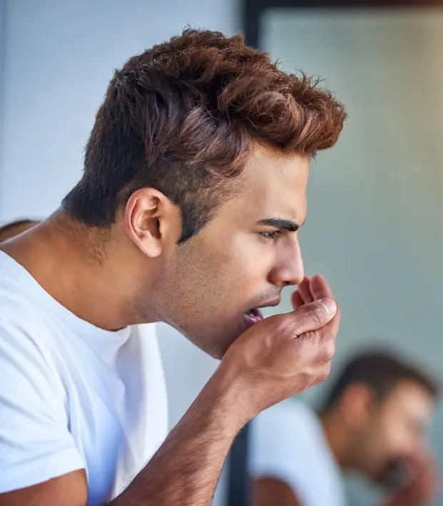 Man with hand near mouth showing concern about bad breath, seeking dental treatment.