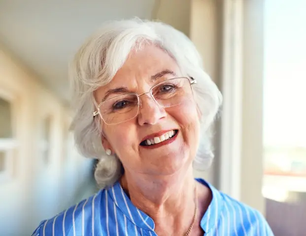 Smiling senior woman wearing glasses and blue shirt in dental office setting.