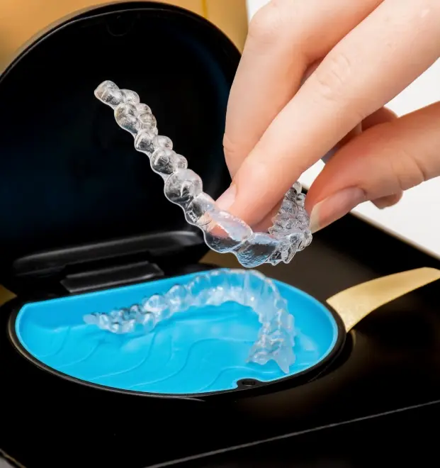 Person holding clear Invisalign aligner tray above blue storage case during orthodontic treatment.