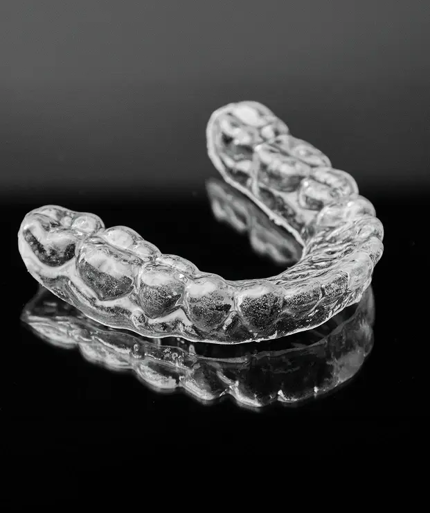 Clear dental night guard and mouthguard displayed on reflective surface.