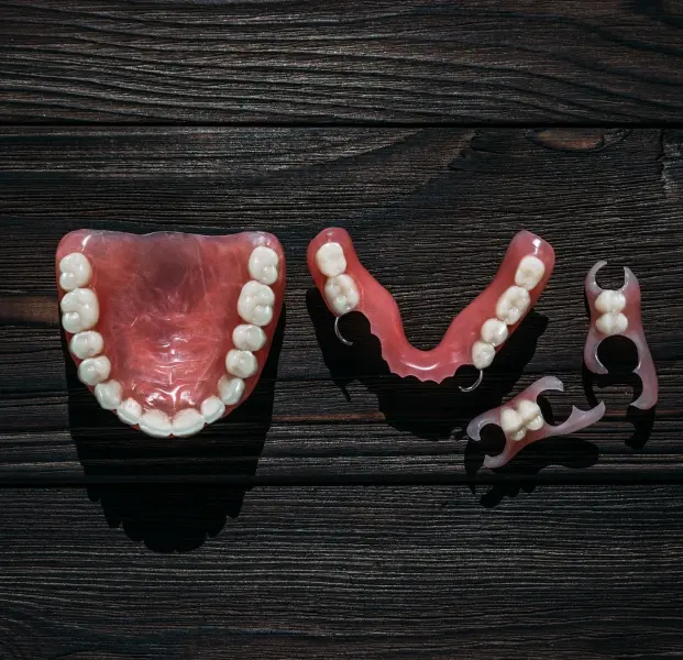 Three partial denture models displaying different designs and tooth arrangements on dark wood.