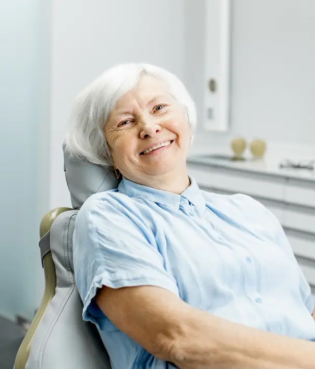 Smiling senior woman patient relaxed in dental chair after root canal treatment.
