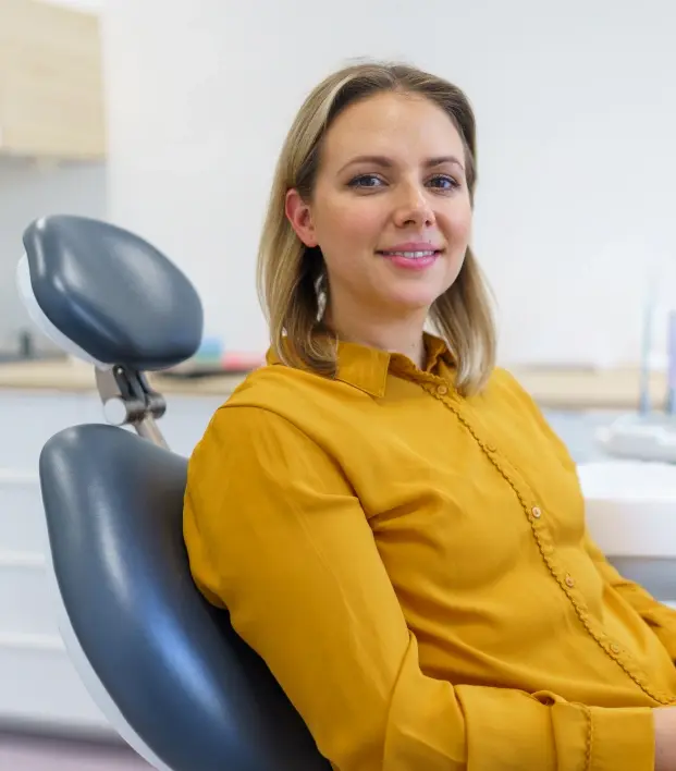 Woman in yellow shirt smiling in dental office treatment room.
