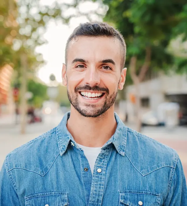 Smiling man in denim shirt showing results of professional teeth whitening treatment.
